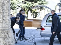 Zamestnanci pohrebnej služby vykladajú rakvu z auta na cintoríne v Bergame