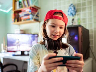 Close up of a Young girl playing games on her smart phone in her bedroom by the desktop computer