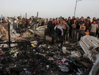 Palestínčania sa pozerajú na zničené miesto po izraelskom útoku, kde sa zdržiavali vysídlení ľudia v Rafahu v pásme Gazy v pondelok 27. mája 2024.