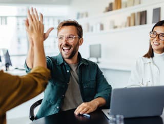 Successful business people giving each other a high five in a meeting. Two young business professionals celebrating teamwork in an office.