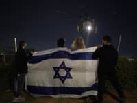 Ľudia s izraelskou vlajkou sledujú prílet vrtuľníka, ktorý preváža izraelských rukojemníkov prepustených Hamasom, do zdravotníckeho centra Sheba v izraelskom meste Ramat Gan v utorok 28. novembra 2023.