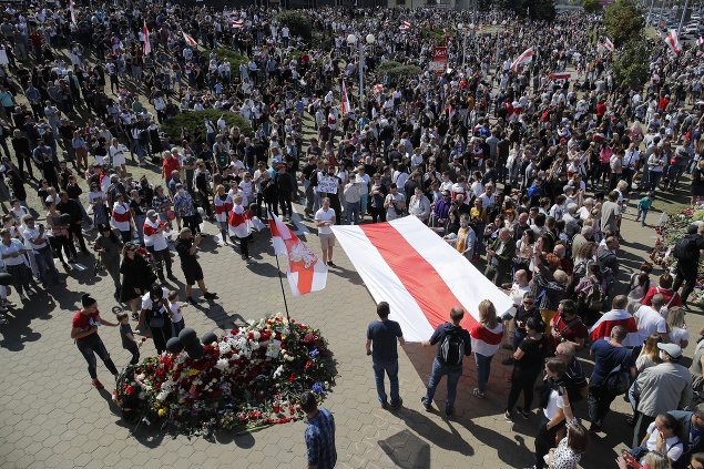 Ľudia držia starú bieloruskú vlajku a kladú kvety na miesto, kde zahynul tento týždeň Alexander Tarajkovski počas zrážok medzi protestujúcimi a policajtmi 15. augusta 2020 v Minsku.