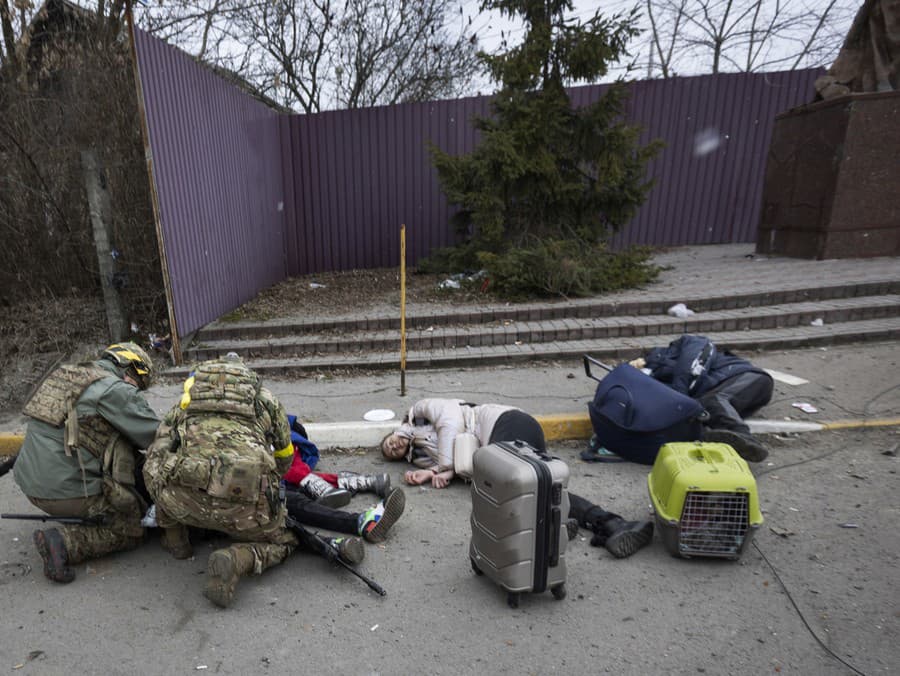 Ukrajinskí  vojaci pomahajú zraneným ľuďom ležiacim na ceste po ruskom ostreľovaní v meste Irpiň