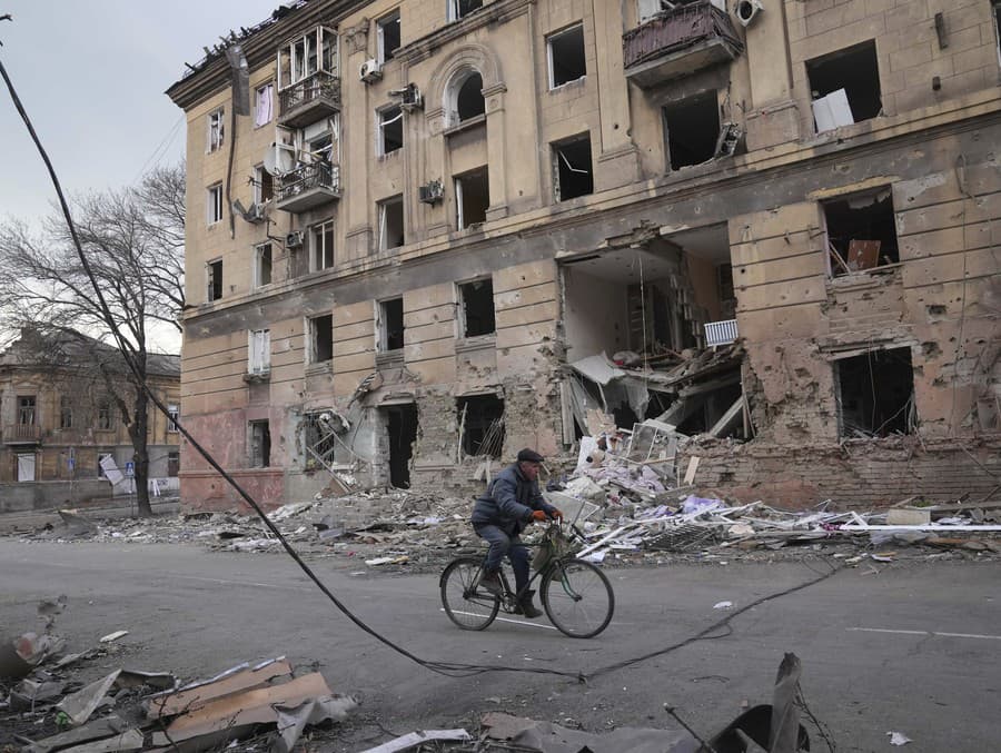 Muž na bicykli v Mariupole prechádza okolo zbombardovanej budovy.