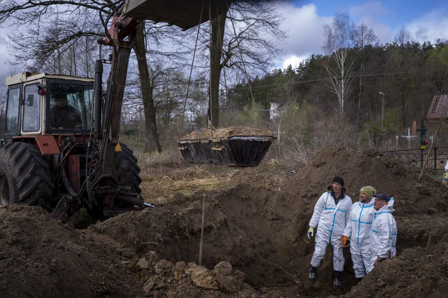 Žeriav dvíha rakvu počas toho, akodobrovoľníci odstraňujú zeminu z masového hrobu počas exhumácie štyroch civilistov zabitých v Mykulychi