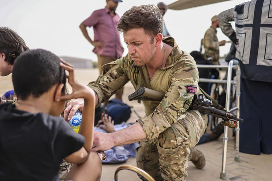 Evakuácia obyvateľov Sudánu. Príslušník štátnej armády ponúka vodu malým deťom na vojenskom letisku. 