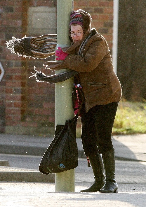 Staršia pani sa len s námahou drží pouličnej lampy počas vyčíňania silného vetra v britskom South Shield.