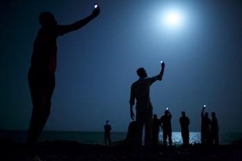 Na snímke z 26. februára 2013 africkí prisťahovalci chytajú v noci na telefónoch lacnejší signál zo susedného Somálska v meste Džibuti, v africkom štáte Džibutsko.