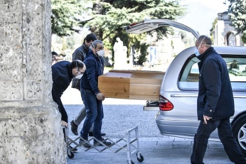 Zamestnanci pohrebnej služby vykladajú rakvu z auta na cintoríne