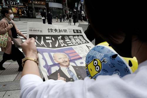 Okoloidúci v Japonsku číta extra vydanie novín Yomiuri s Joeom Bidenom na titulnej strane