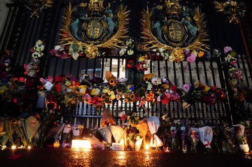 Kvety a zapálené sviečky pred hlavnou bránou Buckinghamského paláca. 
