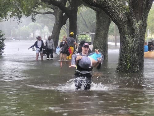 Hasiči pomáhajú ľuďom do bezpečia na zaplavenej ulici v meste Orange County na Floride.