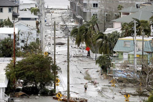 Muž kráča cez ulicu posiatu troskami zo zničených domov a obchodov v meste Fort Myers na Floride.