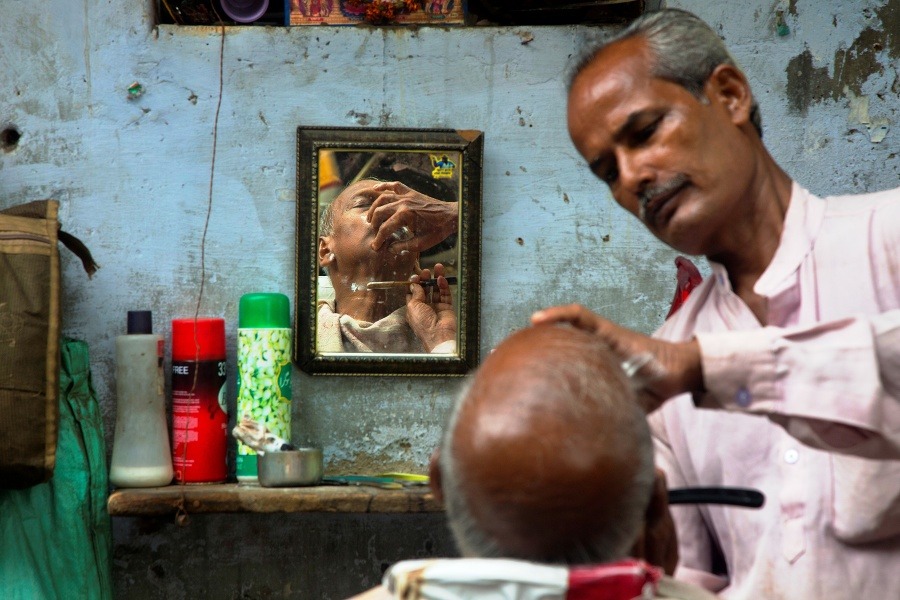 Pouličný holič holí zákazníka v tarej štvrti indickej metropoly Naí Dillí.