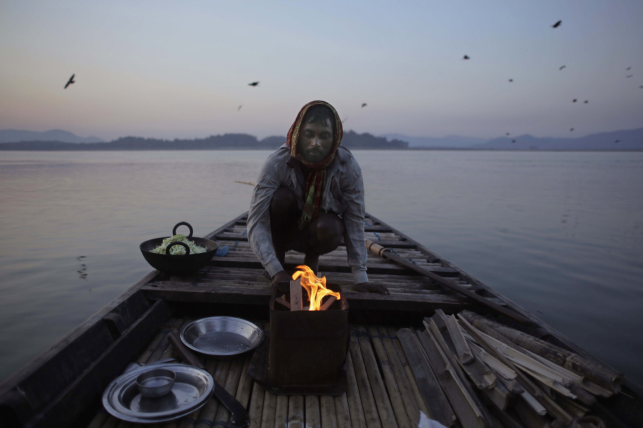 Na snímke indický rybár zapaľuje oheň na varenie jedla pred lovom v člne na rieke Brahmaputre v indickom Gauhátí.