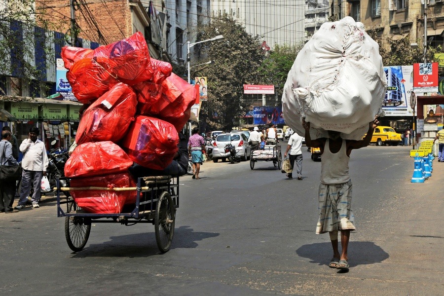 Muž nesie obrovské vrece na hlave idúc okolo plne naloženej rikše s tovarom v indickej Kalkate.