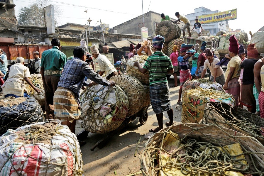 Robotníci prenášajú veľké vrecia zeleniny z nákladných automobilov pri veľkoobchodnom trhu v Kalkate.