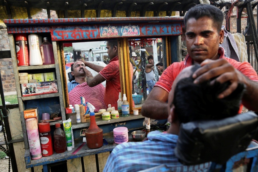 Indický pouličný holič utiera tvár zákazníkovi po oholení v Naí Dillí.