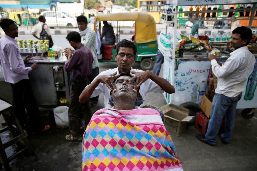 Indický pouličný holič masíruje tvér zákazníkovi v Naí Dillí.