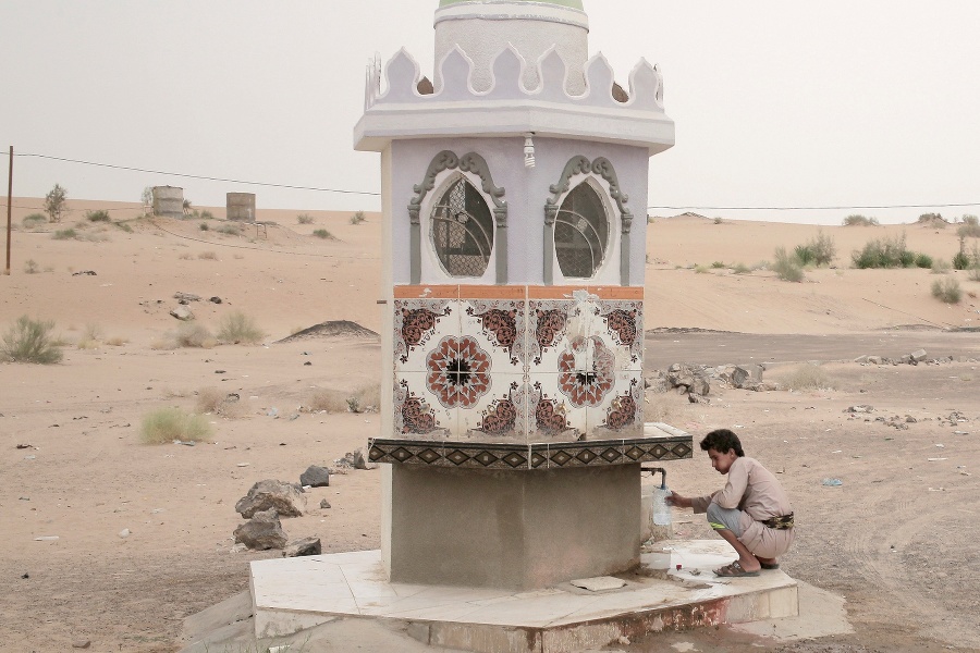 Chlapec naberá vodu z fontánky pri ceste, Marib