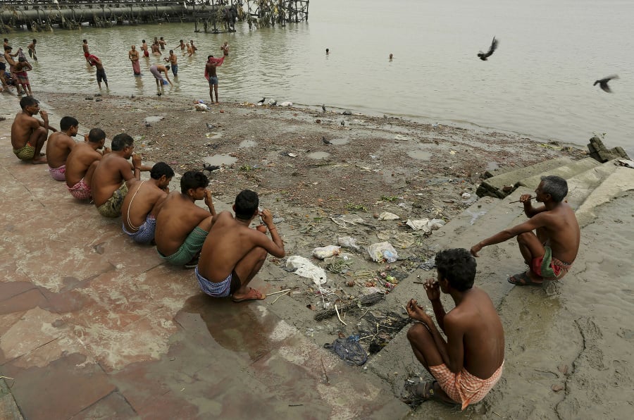 Muži sedia na brehu rieky Huglí a čistia si zuby skoro ráno v Kalkate.