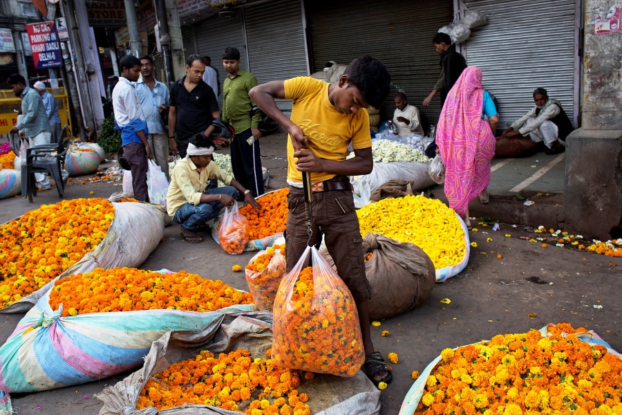 Pouličný predavač kvetín váži kvety v sáčku v skorých ranných hodinách v starej časti metropoly Naí Dillí.