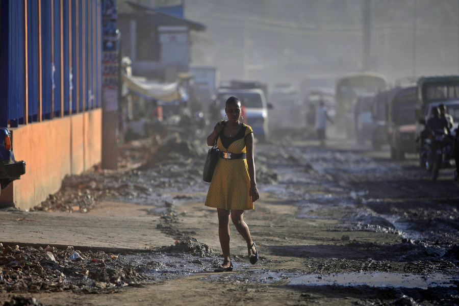 Žena v šatách kráča po zablatenom chodníku v Port-au-Prince.