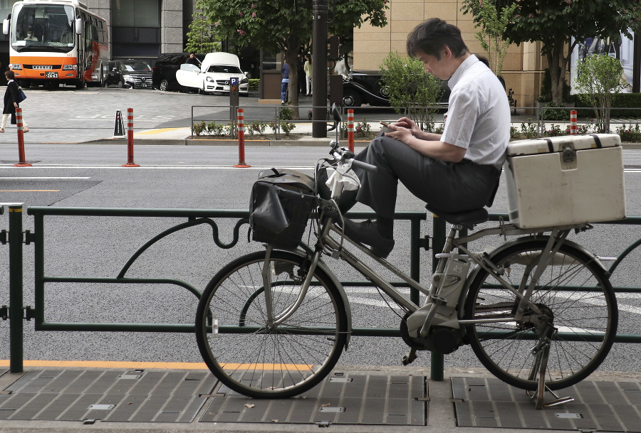 Muž si prezerá mobil sediac na bicykli v tokijskej nákupnej štvrti Ginza.