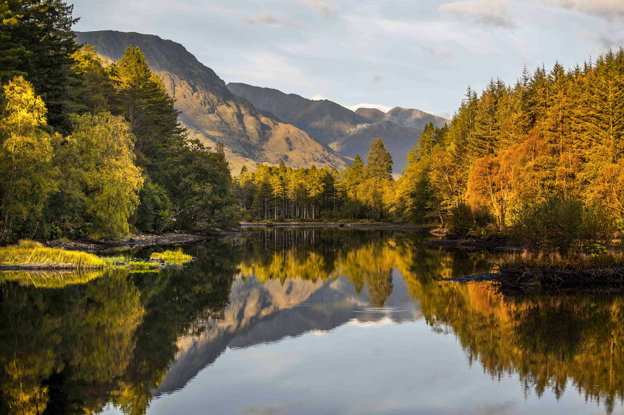 Jeseňou sfarbené stromy sa odrážajú na nehybnej hladine jazera v pralese Glencoe Lochan v Škótsku. © SITA/AP