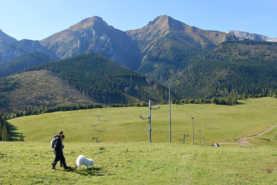 Turisti sa prechádzajú po lúke pod najvyššími štítmi Belianskych Tatier, Ždiarska vidla (2 142 metrov nad morom - vľavo) a Havran (2 152 metrov nad morom) v obci Ždiar.