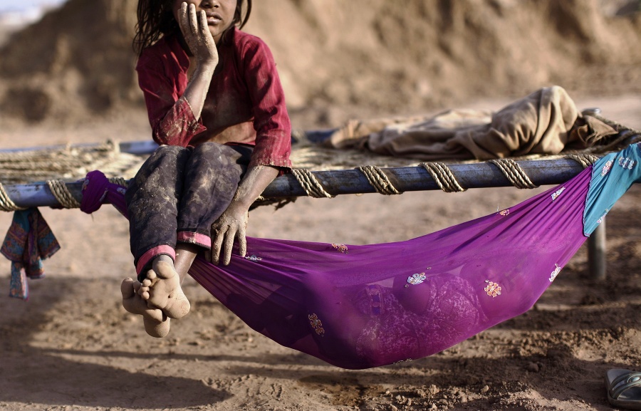 Päťročná Naginah, ktorá pracuje v tehelni, oddychuje na drevenej posteli vedľa svojej osemmesačnej sestry ležiacej v húpacej sieti v pakistanskom Islamabáde.