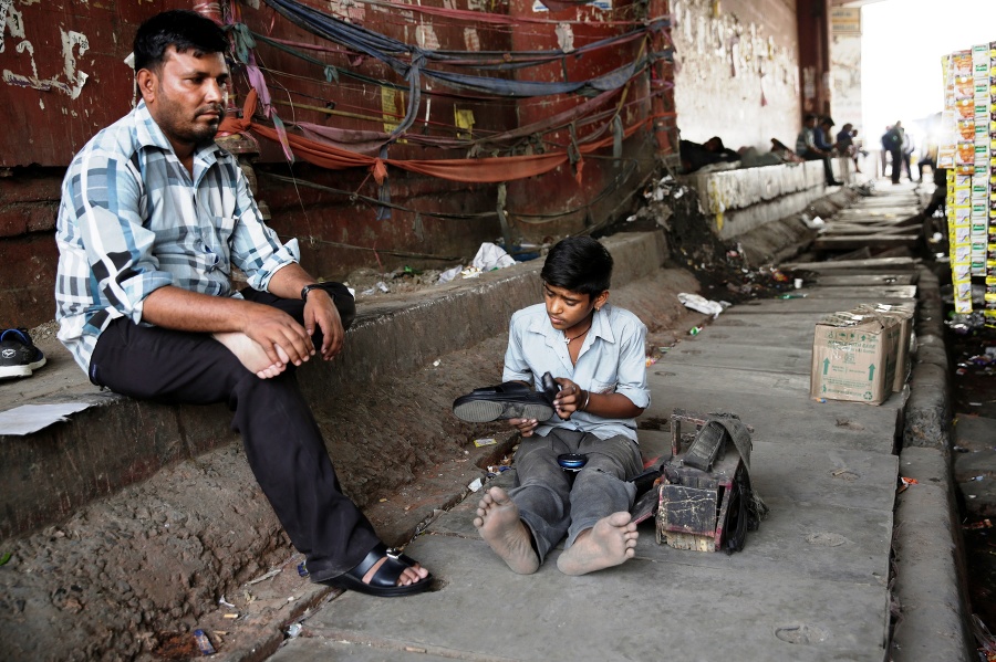 Mladý indický pouličný čistič topánok obsluhuje zákazníka v Naí Dillí.
