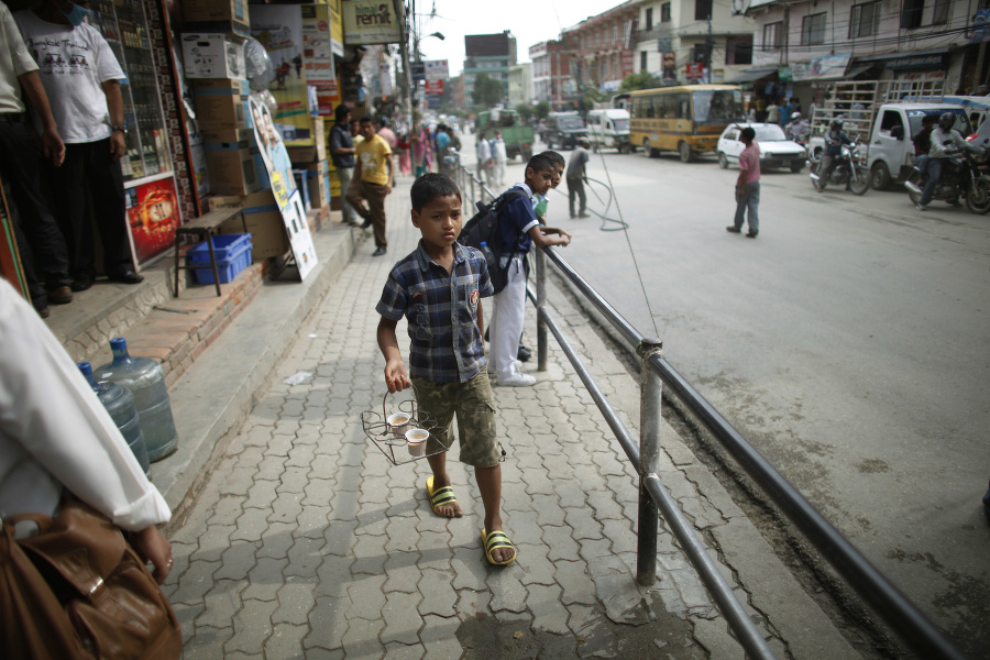 Chlapec nesie čaj zákazníkovi a prechádza okolo školákov, ktorí čakajú na autobus v Káthmadu.