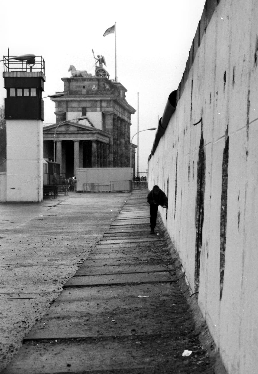 Na archívnej snímke muž prelieza cez otvor v Berlínskom múre.