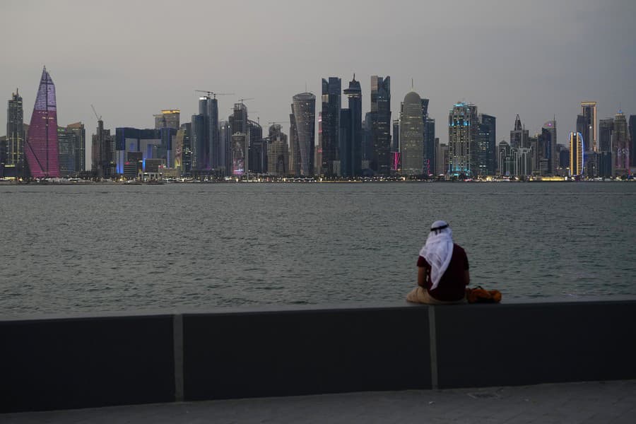 Muž v tradičnom arabskom odeve sedí na promenáde a pozerá sa na mrakodrapy z pobrežia.