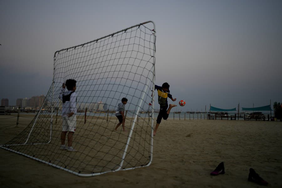 Deti hrajú futbal na pláži Katara v Dauhe.