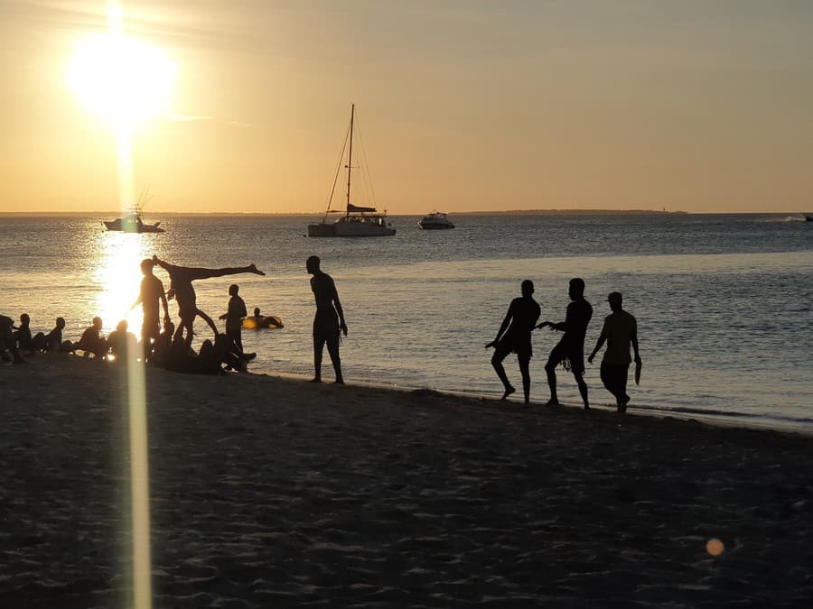 Miestni mladíci tancujú pri západe slnka na pláži Kendwa
