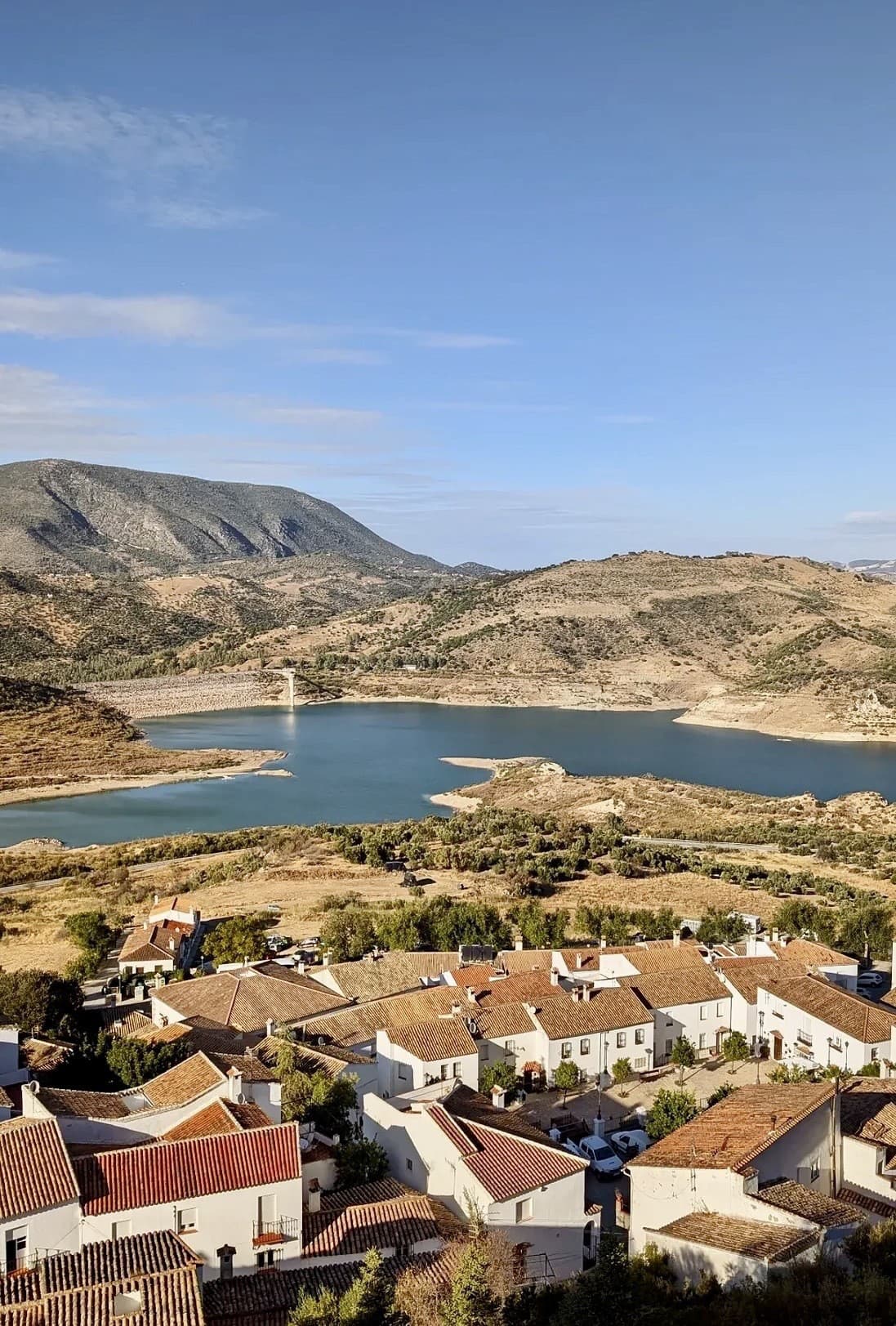 Biela dedina vystavaná na svahu, nad ktorou sa týči starý hrad a pod ňou sa rozprestiera tyrkysové jazero