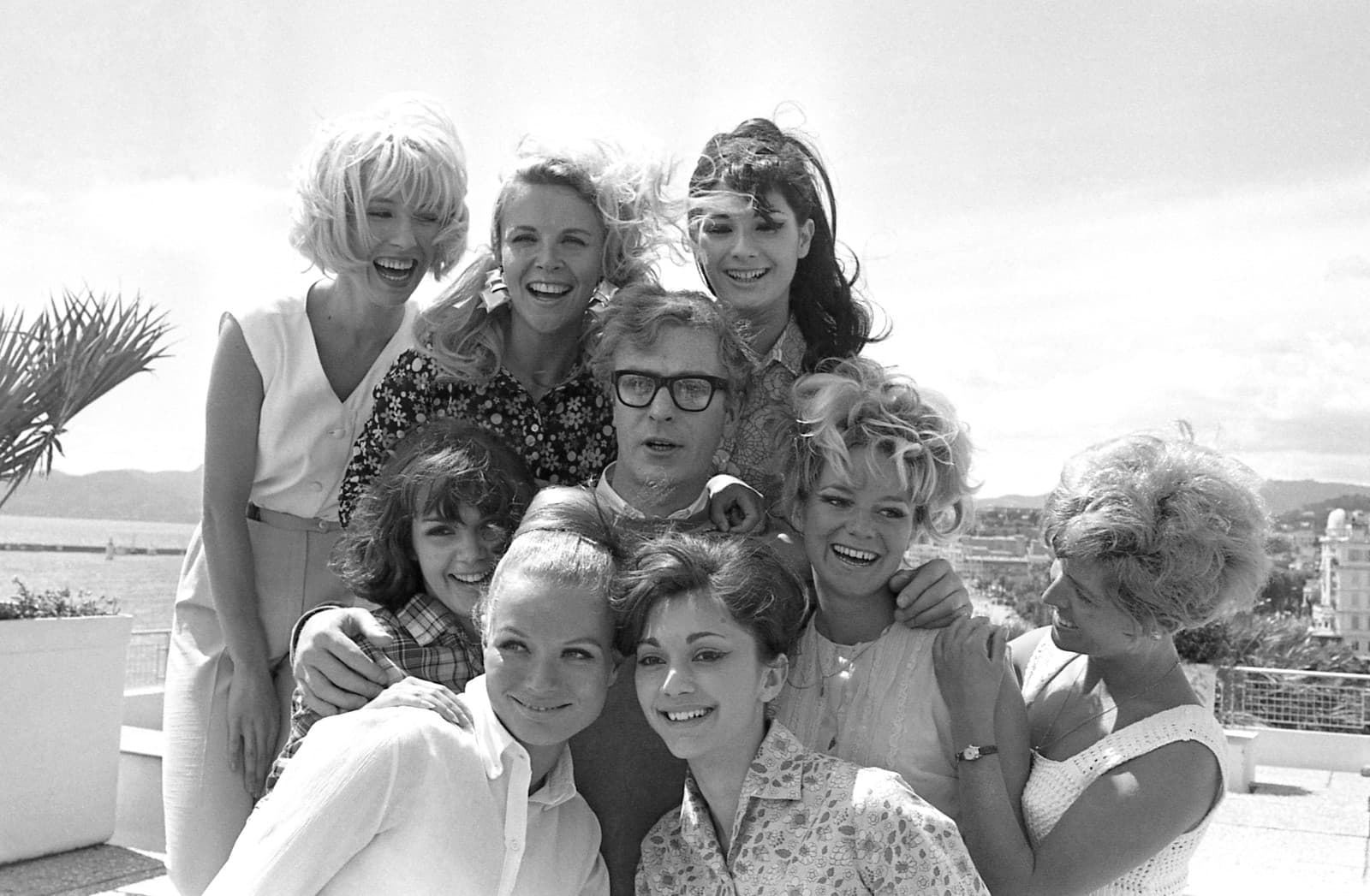 Na archívnej snímke z 9. mája 1966 herec Michael Caine pózuje so skupinou dievčat po tlačovej konferencii k filmu Alfie na Medzinárodnom filmovom festivale v Cannes. (Zdroj: TASR/AP Photo/Jean Jacques Levy, File)