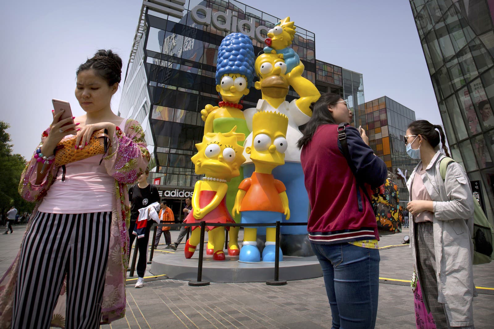 Návštevníci stoja neďaleko sôch zobrazujúce postavičky z kresleného seriálu Simpsonovci v nákupnom centre v Pekingu (Zdroj: TASR/AP Photo/Mark Schiefelbein)